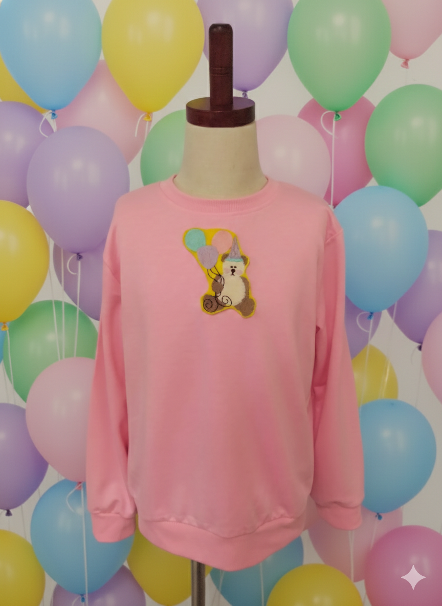Suéter rosa con parche bordado de osito de fiesta